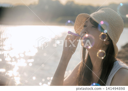 一位身穿白色洋裝的女子在閃爍的燈光下吹著肥皂泡。 一位身穿白色洋裝的女子在閃爍的燈光下吹著肥皂泡。 141494898