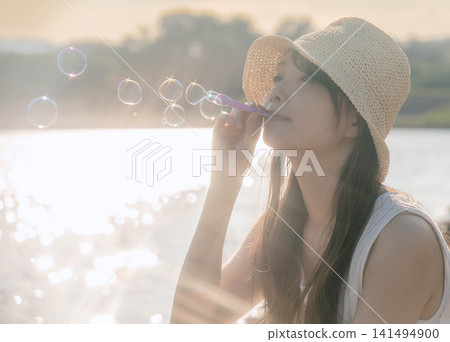 夏日黃昏,一位女子吹肥皂泡,她的側臉出現在鏡頭中。 夏日黃昏,一位女子吹肥皂泡,她的側臉出現在鏡頭中。 141494900