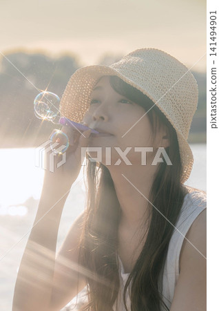一位戴著草帽的女子在燈光下吹肥皂泡。 一位戴著草帽的女子在燈光下吹肥皂泡。 141494901