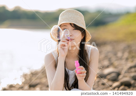 一位戴著草帽的女子在水邊吹肥皂泡。 一位戴著草帽的女子在水邊吹肥皂泡。 141494920