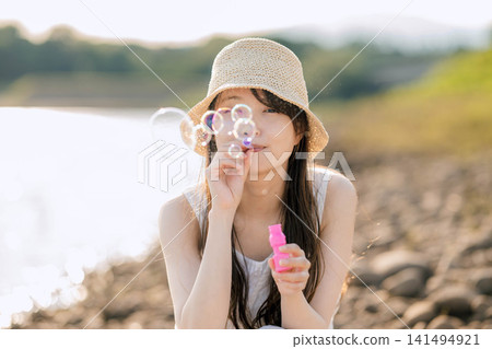 一位身穿白色洋裝的女子在閃爍的燈光下吹著肥皂泡。 一位身穿白色洋裝的女子在閃爍的燈光下吹著肥皂泡。 141494921