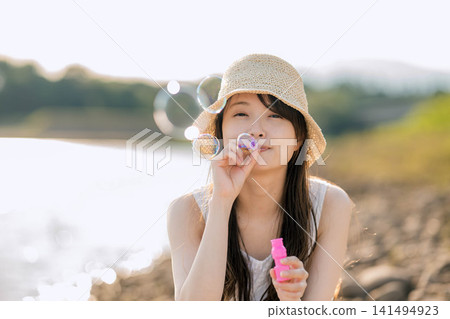 夏天,一位戴著草帽的女子在水邊吹肥皂泡。 夏天,一位戴著草帽的女子在水邊吹肥皂泡。 141494923