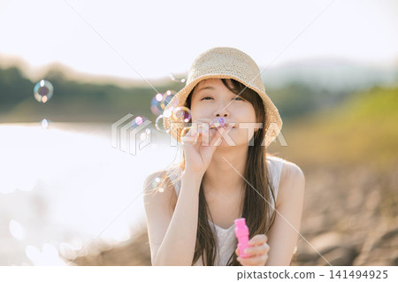 一位身穿白色洋裝的女子在夢幻般的燈光下吹著肥皂泡。 一位身穿白色洋裝的女子在夢幻般的燈光下吹著肥皂泡。 141494925