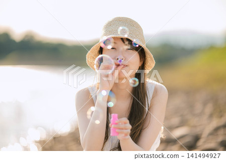 一位女士在波光粼粼的水面上吹肥皂泡。 一位女士在波光粼粼的水面上吹肥皂泡。 141494927