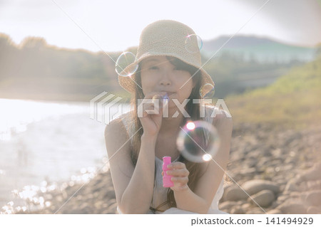 一位戴著草帽的女子在湖邊吹肥皂泡。 一位戴著草帽的女子在湖邊吹肥皂泡。 141494929