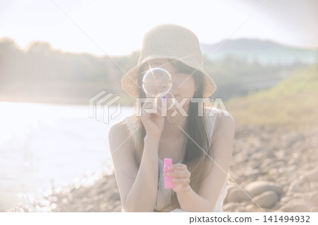 一位身穿白色洋裝的女子正在吹肥皂泡,肥皂泡在逆光下閃閃發光。 一位身穿白色洋裝的女子正在吹肥皂泡,肥皂泡在逆光下閃閃發光。 141494932