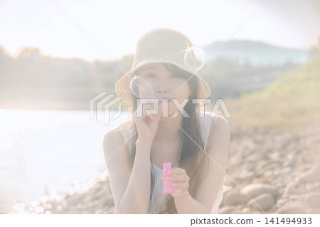一位戴著草帽的女子在水邊吹肥皂泡。 一位戴著草帽的女子在水邊吹肥皂泡。 141494933