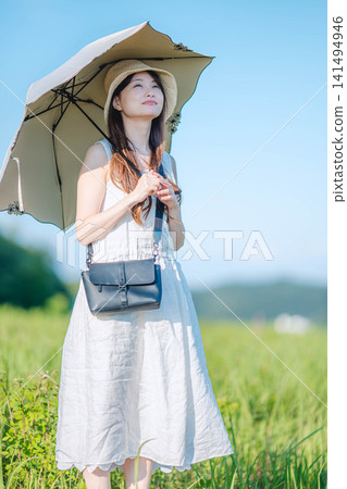 A woman in a white dress stands in a meadow, holding a parasol. A woman in a white dress stands in a meadow, holding a parasol. 141494946