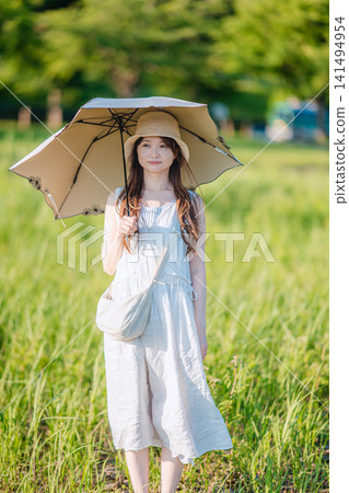 一位女子站在夏日草地上,手持一把陽傘。 一位女子站在夏日草地上,手持一把陽傘。 141494954