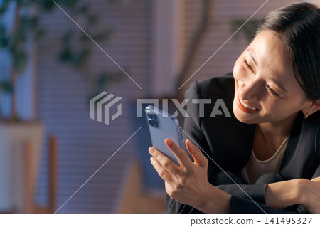 A woman in a suit looking at her smartphone at night. A woman in a suit looking at her smartphone at night. 141495327