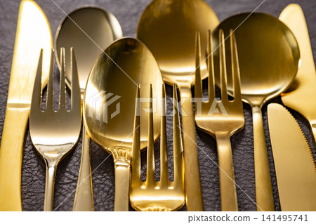 A luxurious dining table adorned with a golden cutlery set, featuring gleaming spoons, forks, and knives. A luxurious dining table adorned with a golden cutlery set, featuring gleaming spoons, forks, and knives. 141495741