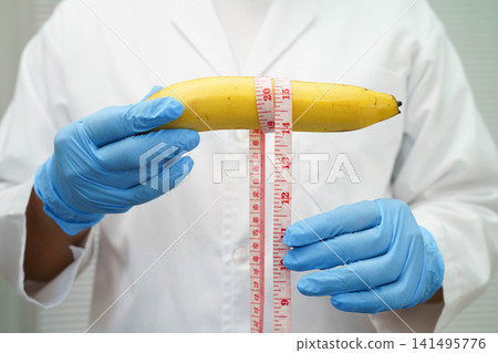 Male doctor stands holding a banana, penis health. Male doctor stands holding a banana, penis health. 141495776