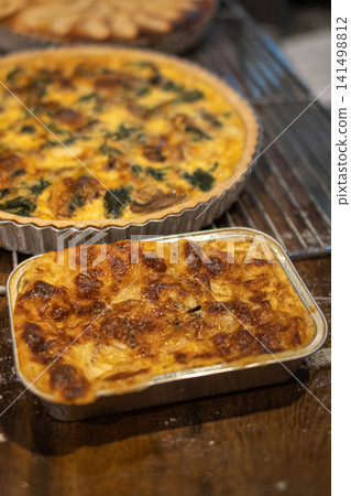 Fresh homemade lasagna with golden baked cheese and mushroom spinach quiche displayed on a rustic wooden table inside a bakery cafe 141498812