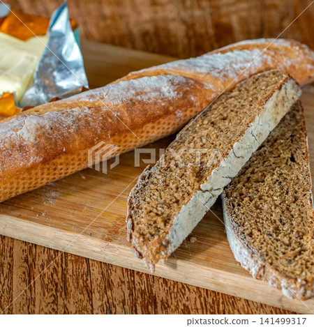Fresh Artisan Baguette and Sliced Whole Grain Bread on Rustic Wooden Cutting Board with Natural Light Fresh Artisan Baguette and Sliced Whole Grain Bread on Rustic Wooden Cutting Board with Natural Light 141499317