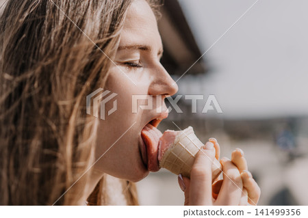 Ice cream woman summer eating strawberry cone outdoors while enjoying sunny weather and holiday vacations Ice cream woman summer eating strawberry cone outdoors while enjoying sunny weather and holiday vacations 141499356