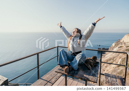 Woman cliff ocean sitting on a wooden table with arms raised at a scenic balcony overlooking the sea feeling joyful Woman cliff ocean sitting on a wooden table with arms raised at a scenic balcony overlooking the sea feeling joyful 141499367