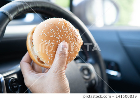 Asian woman driver hold and eat hamburger in car, dangerous and risk an accident. Asian woman driver hold and eat hamburger in car, dangerous and risk an accident. 141500839