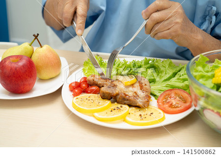 Asian elderly woman patient eating pork chop stake and vegetable salad for healthy food in hospital. Asian elderly woman patient eating pork chop stake and vegetable salad for healthy food in hospital. 141500862