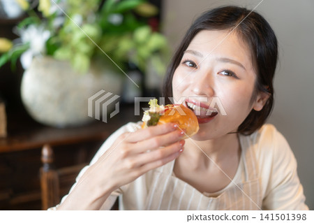 A young woman eating a sandwich at a guesthouse in a traditional Japanese-style house. 141501398