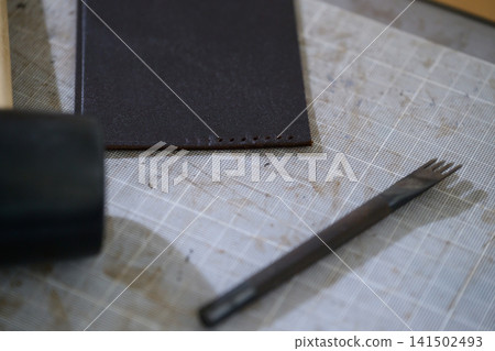 A four-pronged diamond awl and rubber hammer for leather crafting are placed on the table. A four-pronged diamond awl and rubber hammer for leather crafting are placed on the table. 141502493