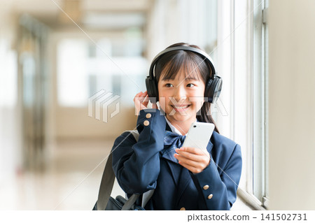 小學、國中、高中女生穿著校服在學校走廊上戴著耳機聽音樂 小學、國中、高中女生穿著校服在學校走廊上戴著耳機聽音樂 141502731