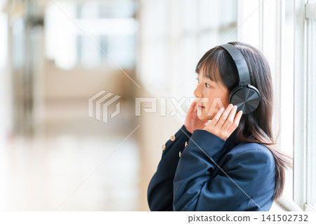 小學、國中、高中女生穿著校服在學校走廊上戴著耳機聽音樂 小學、國中、高中女生穿著校服在學校走廊上戴著耳機聽音樂 141502732