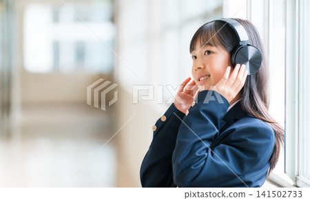 小學、國中、高中女生穿著校服在學校走廊上戴著耳機聽音樂 小學、國中、高中女生穿著校服在學校走廊上戴著耳機聽音樂 141502733