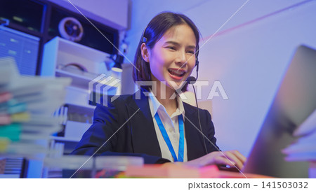 Smiling young Asian customer service representative wearing microphone headset and working on laptop Smiling young Asian customer service representative wearing microphone headset and working on laptop 141503032