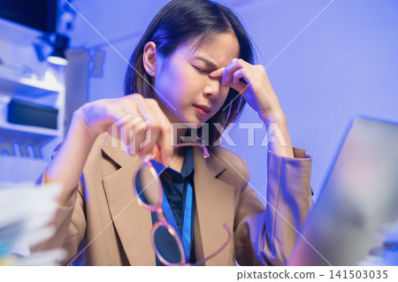 Young Asian businesswoman suffering from eye strain while working on laptop in office. Young Asian businesswoman suffering from eye strain while working on laptop in office. 141503035