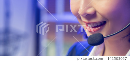 Smiling young Asian customer service representative wearing microphone headset and working on laptop 141503037