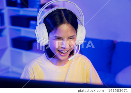 Young Asian woman playing online computer game with headset at home, esports and live streaming concept. Young Asian woman playing online computer game with headset at home, esports and live streaming concept. 141503671