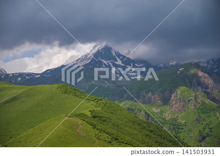 Mount Kazbek in stormy clouds above green ridges of Caucasus with copy space Mount Kazbek in stormy clouds above green ridges of Caucasus with copy space 141503931