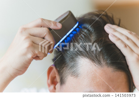 A man using an electric brush to care for his scalp. A man using an electric brush to care for his scalp. 141503973