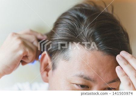 A man in his 40s uses an electric brush to care for his graying hair. A man in his 40s uses an electric brush to care for his graying hair. 141503974