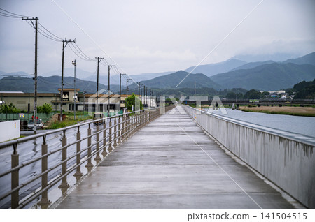 在陰雨綿綿的天空下,一條沿著嶄新海堤的小路延伸到遠方,遠處可以看到電線桿和連綿的山脈。 在陰雨綿綿的天空下,一條沿著嶄新海堤的小路延伸到遠方,遠處可以看到電線桿和連綿的山脈。 141504515