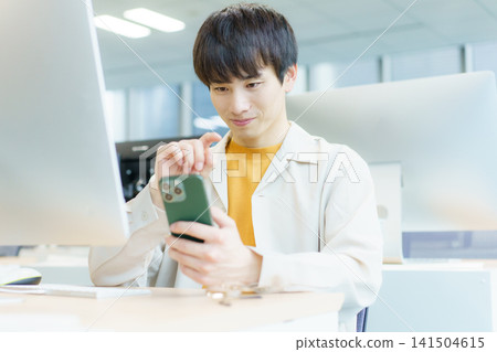 一位年輕的日本男子坐在桌前操作智慧型手機。照片由東京電子學院電波學園教育基金會提供。 一位年輕的日本男子坐在桌前操作智慧型手機。照片由東京電子學院電波學園教育基金會提供。 141504615