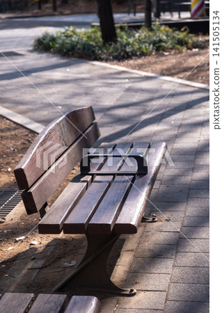 Close up of wooden bench, with pathway on the background in public park Close up of wooden bench, with pathway on the background in public park 141505134