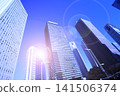 A cluster of skyscrapers and a cluster of high-rise office buildings bathed in sunlight. 141506374