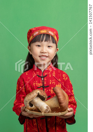 Smiling Young Chinese Girl in Traditional Red Ethnic Costume Holding Large Mushrooms; Happy Asian Child Presenting Fresh Harvest on Green Background; Healthy Organic Food and Cultural Heritage Smiling Young Chinese Girl in Traditional Red Ethnic Costume Holding Large Mushrooms; Happy Asian Child Presenting Fresh Harvest on Green Background; Healthy Organic Food and Cultural Heritage 141507767