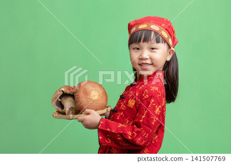 Smiling Young Chinese Girl in Traditional Red Ethnic Costume Holding Large Mushrooms; Happy Asian Child Presenting Fresh Harvest on Green Background; Healthy Organic Food and Cultural Heritage Smiling Young Chinese Girl in Traditional Red Ethnic Costume Holding Large Mushrooms; Happy Asian Child Presenting Fresh Harvest on Green Background; Healthy Organic Food and Cultural Heritage 141507769