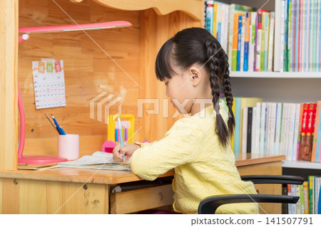 Asian little girl studying at wooden desk, back view child doing homework at home, cozy study environment concept 141507791