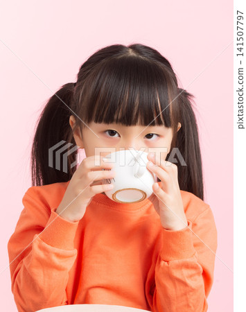 Asian little girl drinking from cup, child enjoying beverage on pink background, lifestyle and refreshment concept Asian little girl drinking from cup, child enjoying beverage on pink background, lifestyle and refreshment concept 141507797