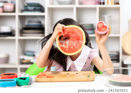 Cute Asian girl making fun shapes with watermelon in kitchen, happy emotion, healthy eating and childhood creativity concept Cute Asian girl making fun shapes with watermelon in kitchen, happy emotion, healthy eating and childhood creativity concept 141507831
