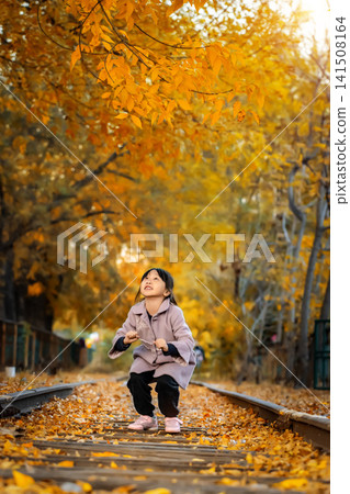Exuberant little girl jumps high into the air on a scenic railway line surrounded by golden autumn trees. 141508164