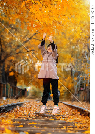 Exuberant little girl jumps high into the air on a scenic railway line surrounded by golden autumn trees. 141508165