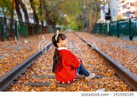 Sweet little girl sits on the railway track and looks back over her shoulder with a bright smile. Sweet little girl sits on the railway track and looks back over her shoulder with a bright smile. 141508184