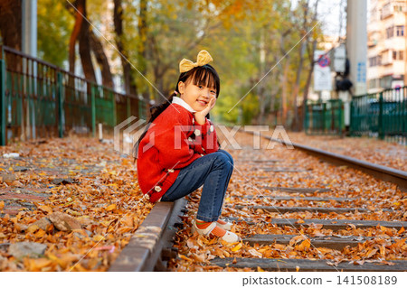 Little girl wearing a red sweater crouches on an old railway track ,On an autumn day Little girl wearing a red sweater crouches on an old railway track ,On an autumn day 141508189