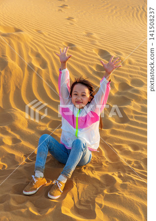 A little girl playing happily on the ground in the desert; the concept of a happy holiday trip. A little girl playing happily on the ground in the desert; the concept of a happy holiday trip. 141508237