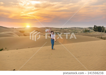 Back view of a little girl walking on a sand dune toward the bright sunset. Back view of a little girl walking on a sand dune toward the bright sunset. 141508238