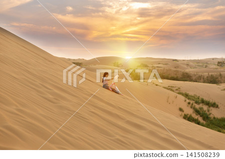 Silhouette of a little girl sitting on a giant sand dune watching the magnificent sunset. Silhouette of a little girl sitting on a giant sand dune watching the magnificent sunset. 141508239